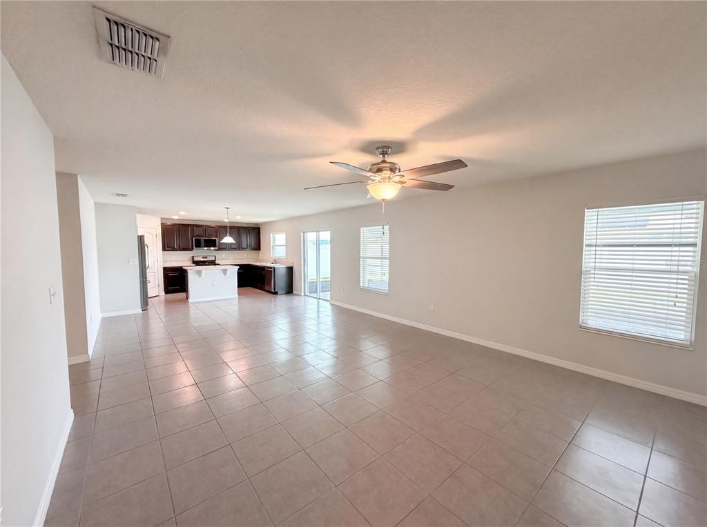 An open-concept living area with tile flooring, a ceiling fan, and a kitchen in back — 4272 MOON SHADOW LOOP, MULBERRY, FL