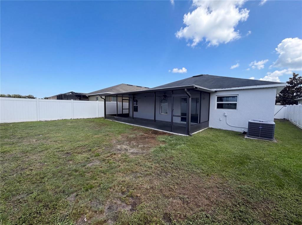 A backyard view of a house with a screened-in patio and a white vinyl fence — 4272 MOON SHADOW LOOP, MULBERRY, FL