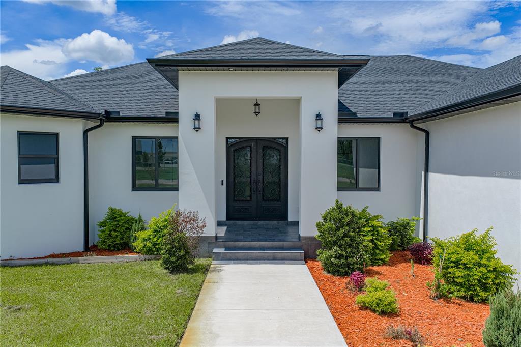 The exterior of a white house features a covered entryway with double doors and landscaping — 14080 SYDNEY ROAD, DOVER, FL