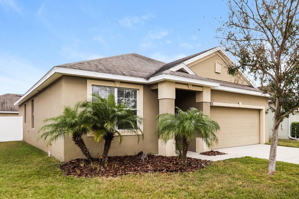 A single-story house with a tan stucco exterior, a two-car garage, and two small palm trees — 925 KRENSON WOODS ROAD, LAKELAND, FL