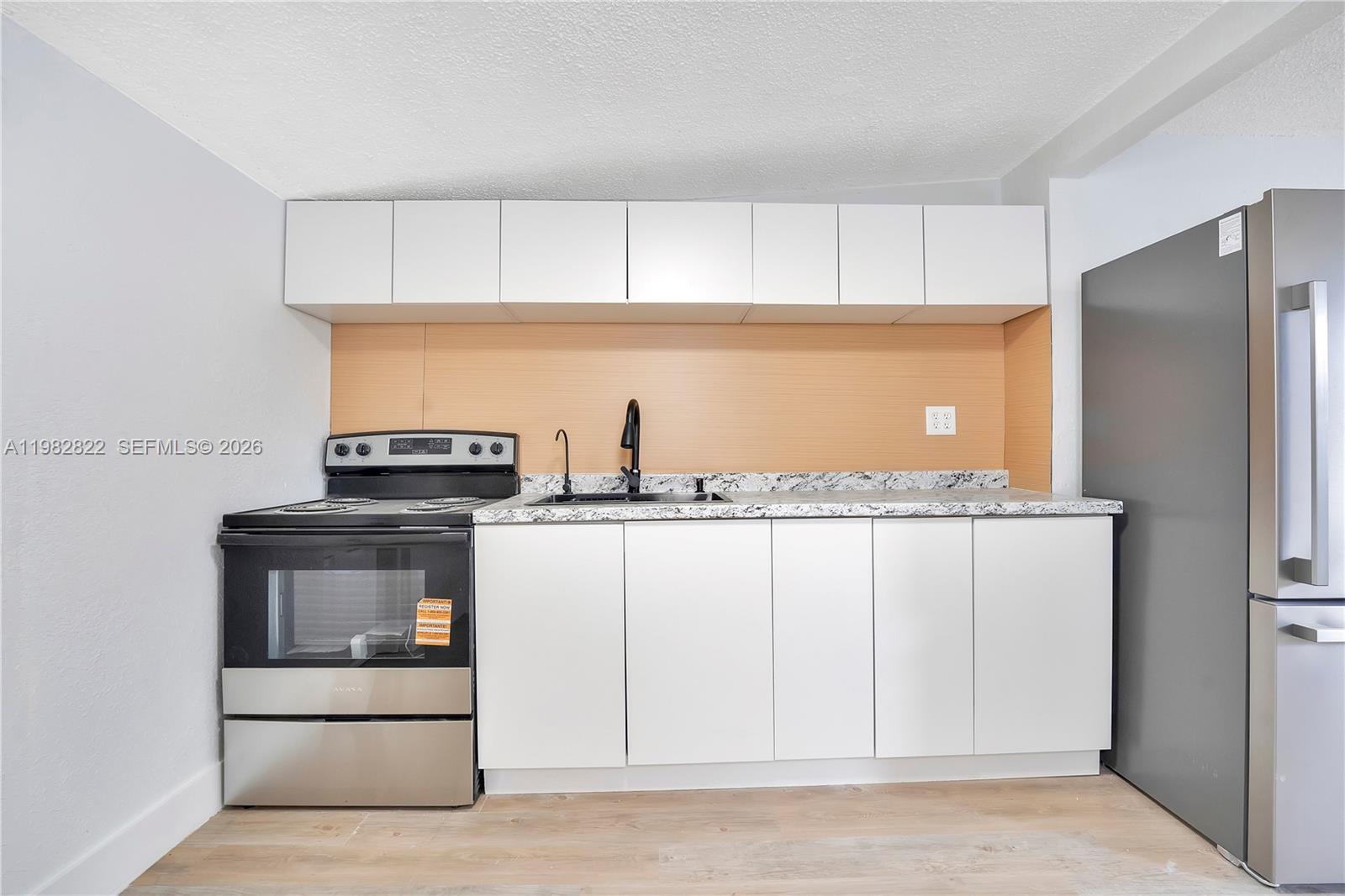 A kitchen features white cabinets, a stainless steel stove, a refrigerator, and a speckled countertop — 2428 NW 28th St REAR, Miami FL 33142, MIAMI, FL