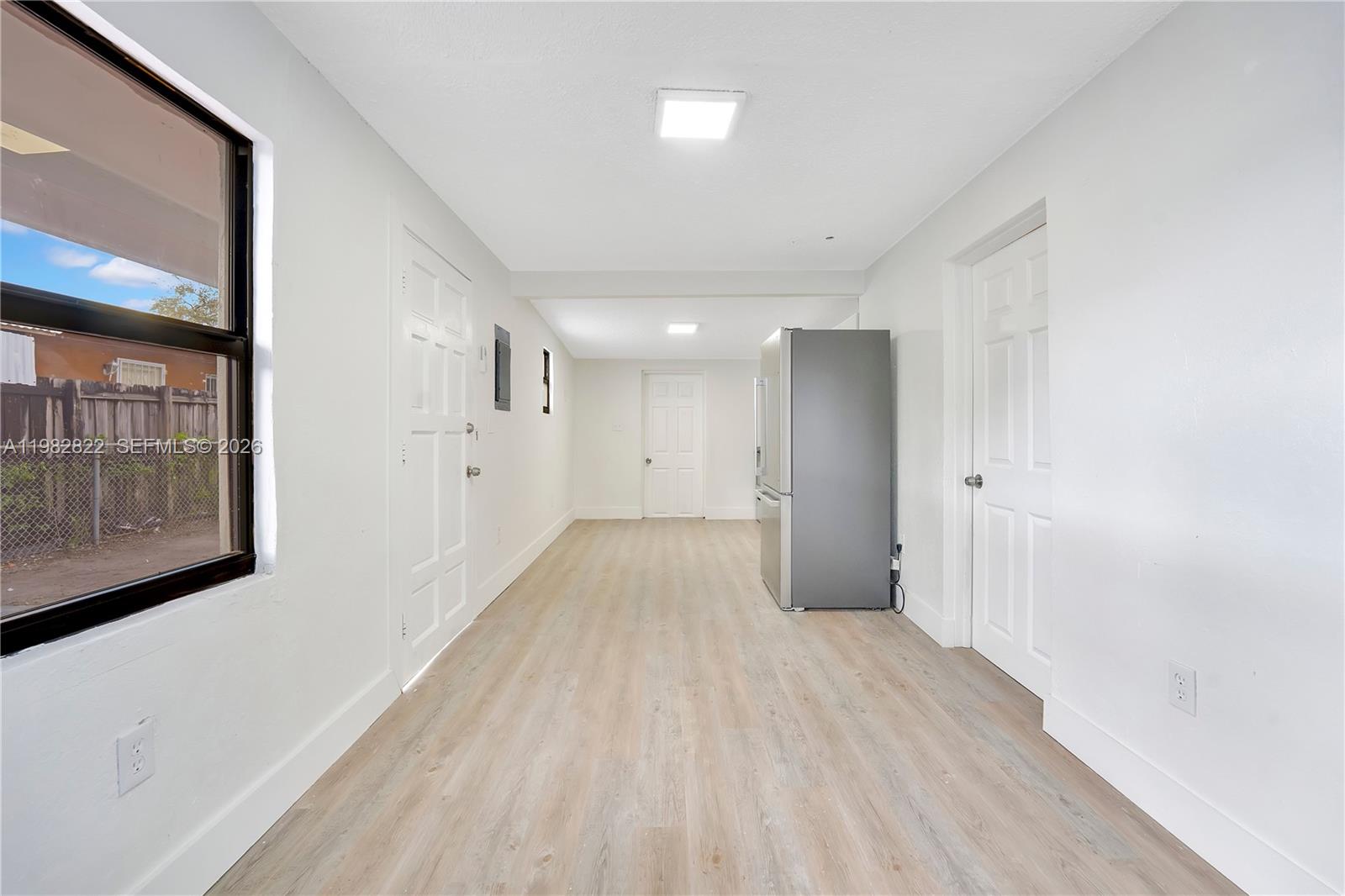 A long, narrow room with white walls, light wood-look flooring, and a stainless steel refrigerator — 2428 NW 28th St REAR, Miami FL 33142, MIAMI, FL