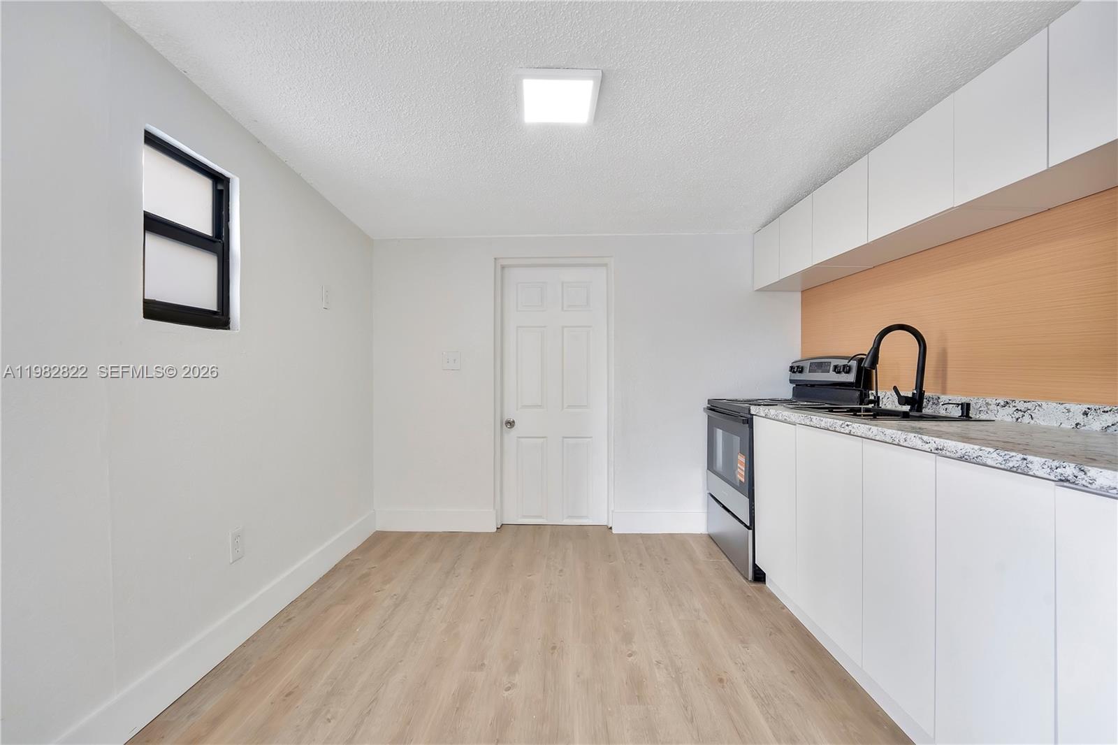 A kitchen features white cabinets, a light wood backsplash, and light-colored wood-look flooring — 2428 NW 28th St REAR, Miami FL 33142, MIAMI, FL