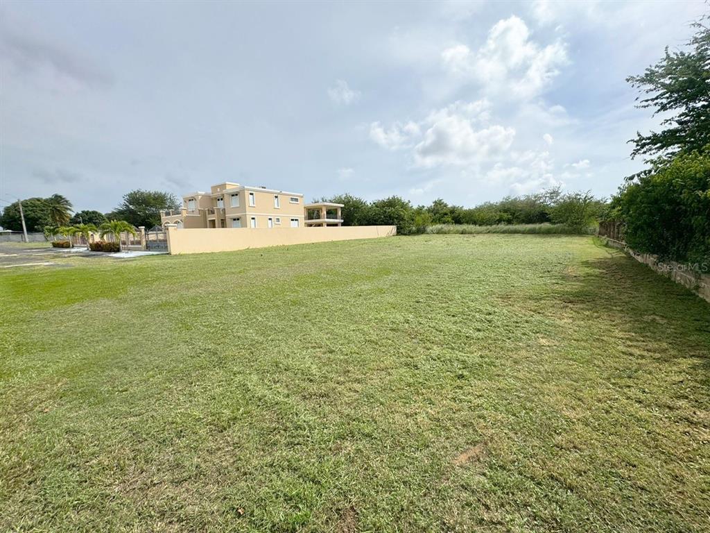 A large, flat, grassy vacant lot sits next to a multi-story tan building — Lot E PR 110 AGUACATE, AGUADILLA, PR