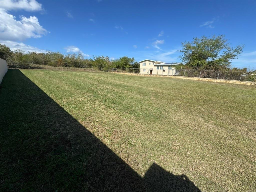 A large, flat, grassy backyard features a chain-link fence and a neighboring house — Lot E PR 110 AGUACATE, AGUADILLA, PR