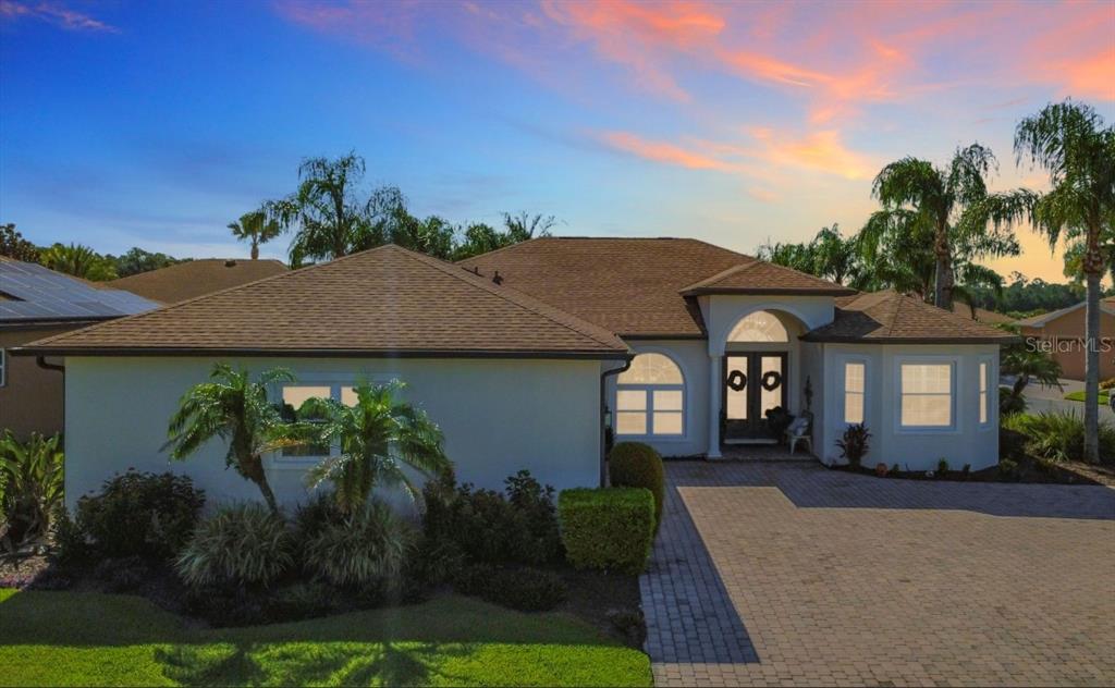 A single-story house with a paved driveway, arched entryway, and palm trees at sunset — 4231 COCONUT DRIVE, LAKE WALES, FL