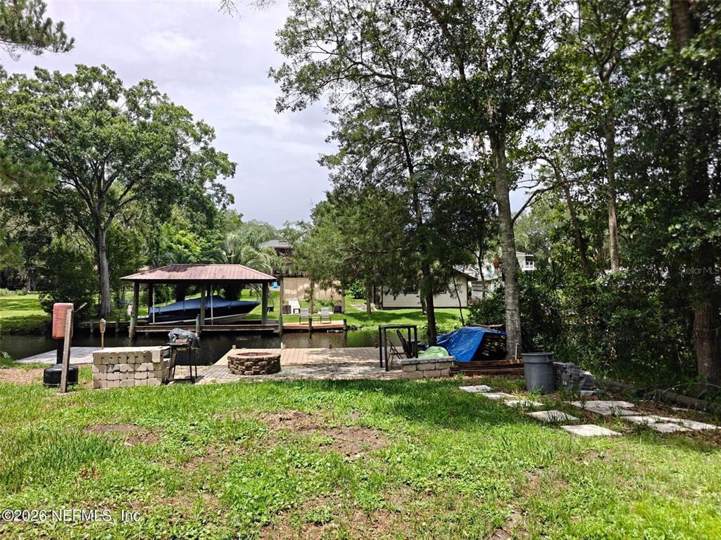 A backyard features a wooden dock, a covered boat slip, and a stone fire pit — 5235 HIDE-A-WAY DRIVE, JACKSONVILLE, FL