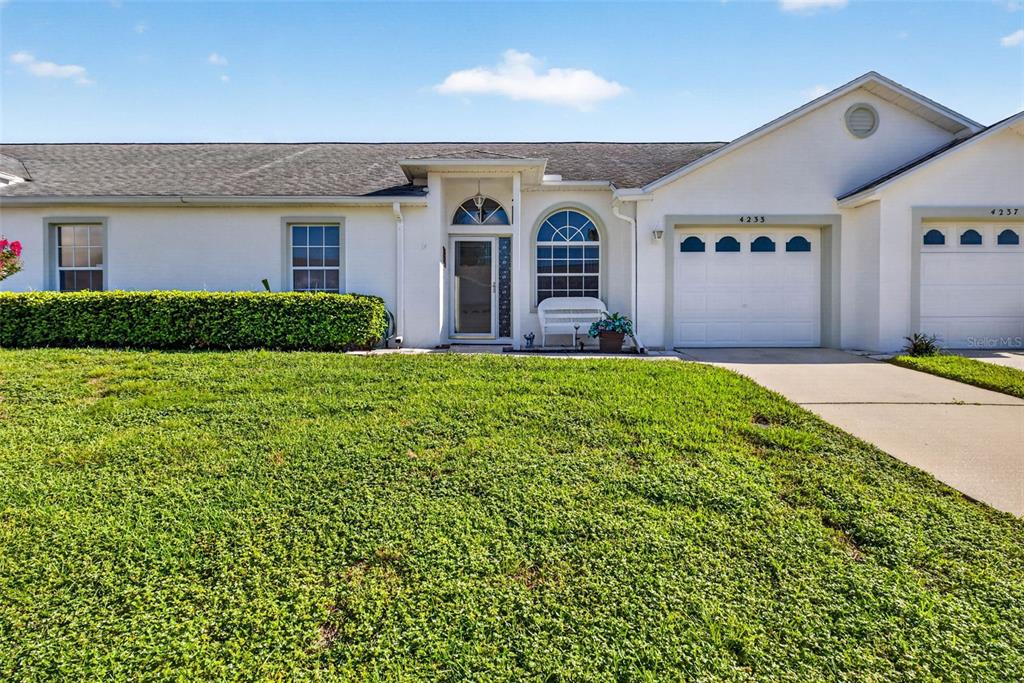 A single-story white house features a front lawn, a garage, and an arched entryway — 4233 AVANTI CIRCLE, NEW PORT RICHEY, FL