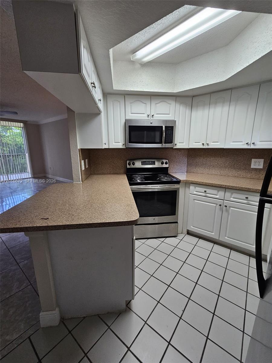 A kitchen features white cabinets, stainless steel appliances, tan countertops, and white tiled flooring — 8245 Lake Dr # 401, Doral FL 33166, DORAL, FL