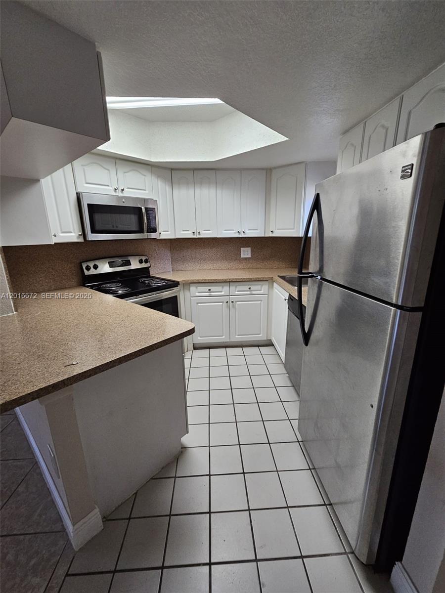 A kitchen features white cabinets, stainless steel appliances, tan countertops, and white tiled flooring — 8245 Lake Dr # 401, Doral FL 33166, DORAL, FL