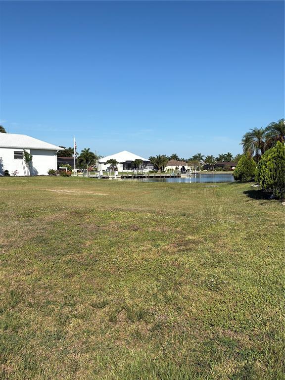 A grassy vacant lot overlooks a canal with houses and palm trees in the distance — 534 MACEDONIA DRIVE, PUNTA GORDA, FL