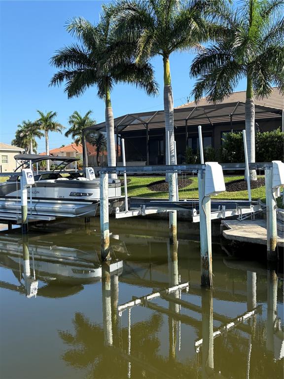 A pontoon boat is docked at a canal-side lift behind a house with palm trees — 534 MACEDONIA DRIVE, PUNTA GORDA, FL
