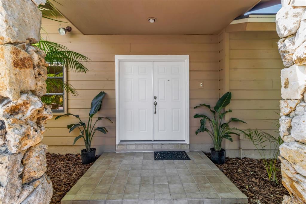 A white double front door is centered on a tiled porch between two stone pillars — 1732 PINE HARRIER CIRCLE, SARASOTA, FL