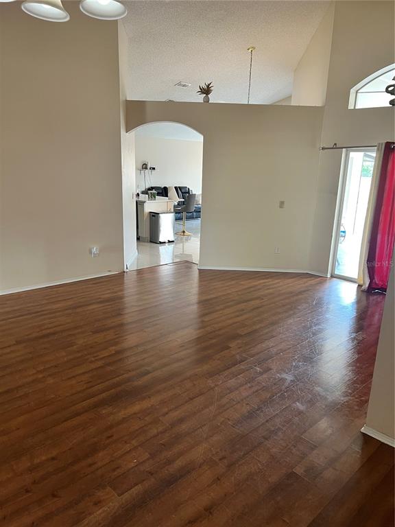 A living room with wood-look flooring leads through an arched doorway to a kitchen area — 801 KAMCHATKA COURT, APOPKA, FL