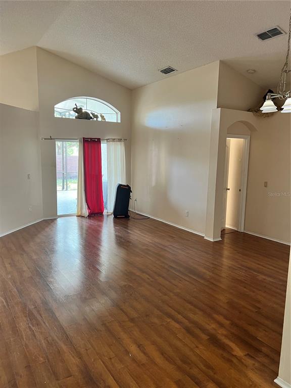 A living room with wood-look flooring, vaulted ceilings, and a sliding glass door — 801 KAMCHATKA COURT, APOPKA, FL