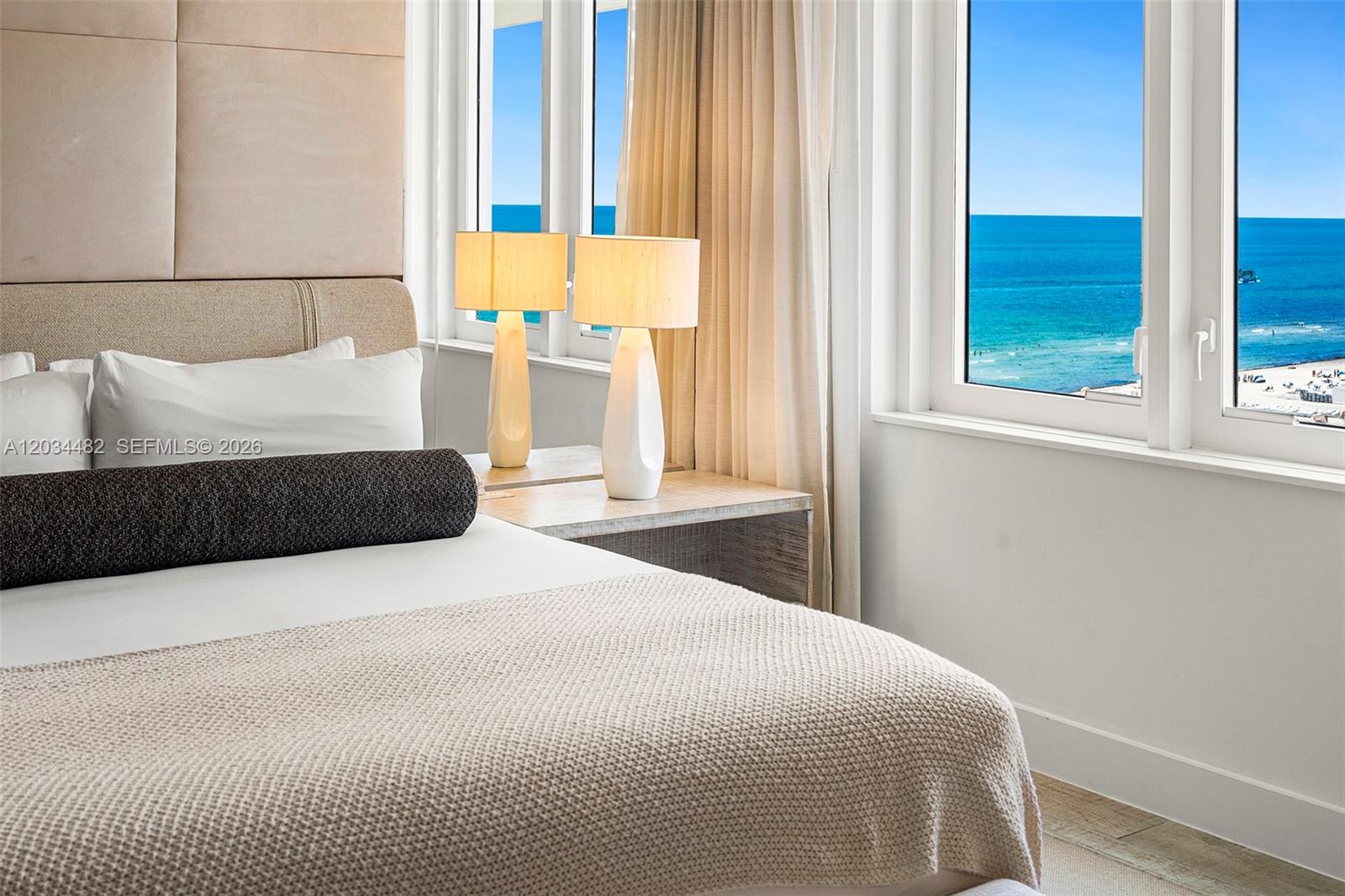 A bedroom features a bed with a textured throw, two lamps, and an ocean view — 102 24th St # 1112, Miami Beach FL 33139, MIAMI BEACH, FL