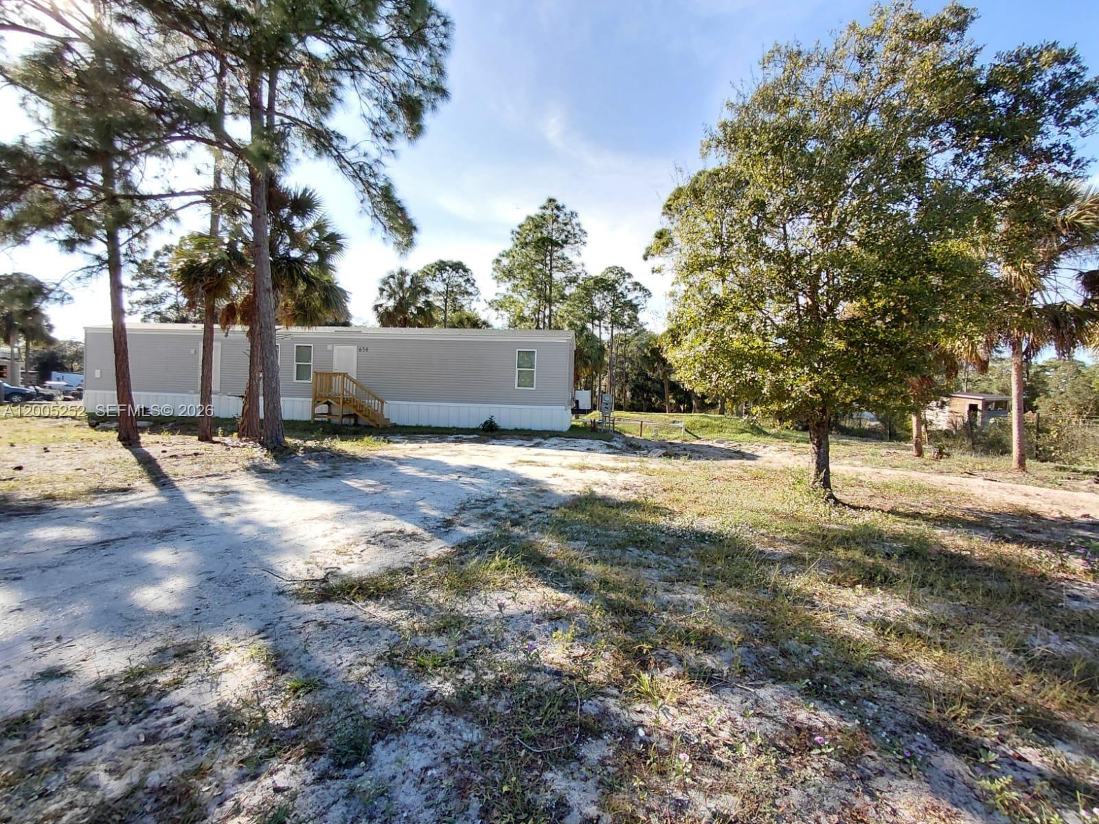 A single-story manufactured home sits on a sandy lot surrounded by trees — 630 S Trebol Street, Clewiston FL 33440, CLEWISTON, FL