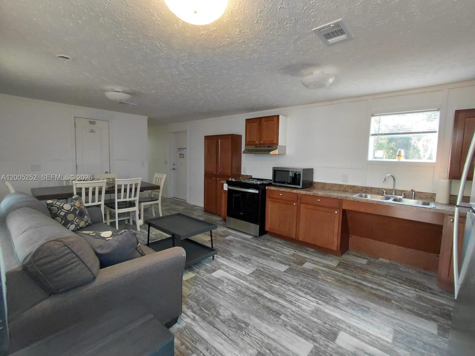This open-concept kitchen and living area features wood-look flooring, wooden cabinets, and a dining set — 630 S Trebol Street, Clewiston FL 33440, CLEWISTON, FL