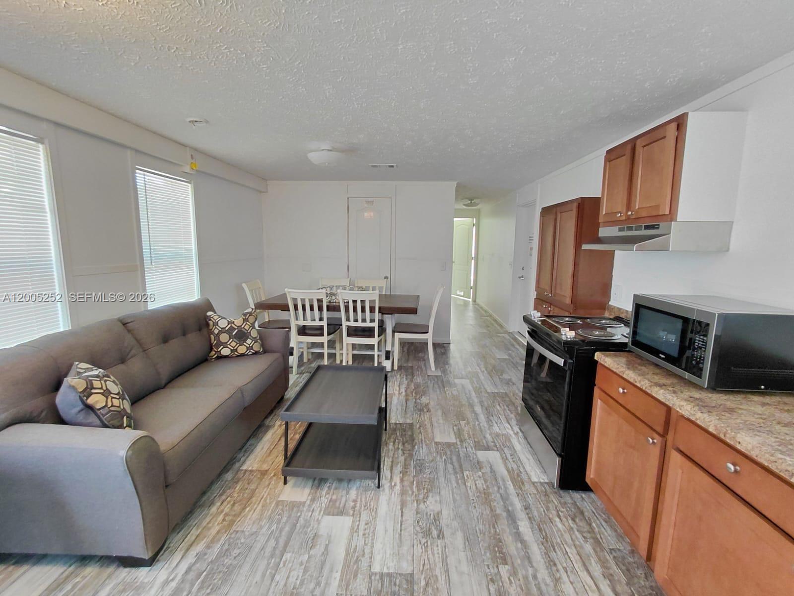 An open-concept living and dining area features wood-look flooring, a gray sofa, and kitchen cabinetry — 630 S Trebol Street, Clewiston FL 33440, CLEWISTON, FL