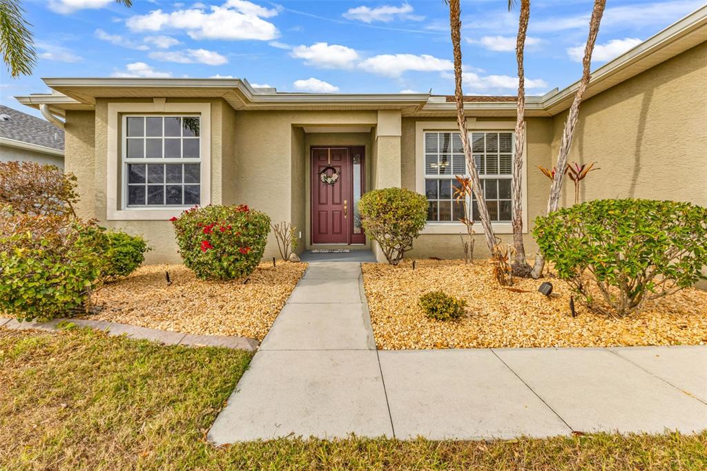 A single-story house exterior features a beige stucco facade, a red front door, and landscaping — 1955 YORKTOWN TRAIL, PUNTA GORDA, FL
