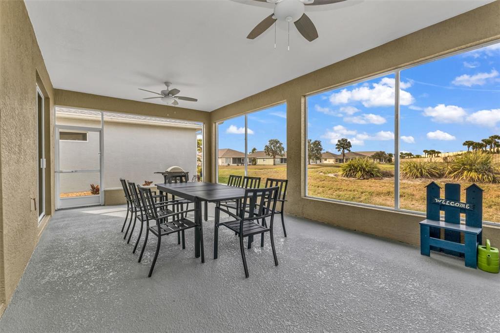 A covered patio features a dining set, ceiling fans, and large screened windows overlooking grass — 1955 YORKTOWN TRAIL, PUNTA GORDA, FL