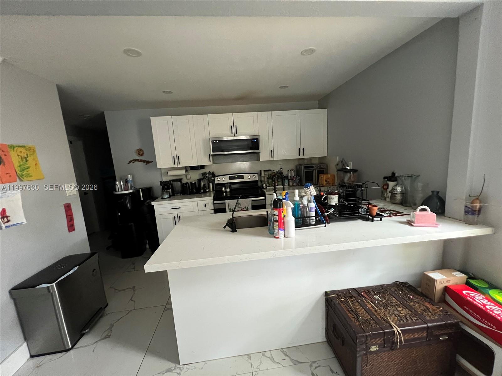 A kitchen features white cabinets, a quartz-topped island, and light-colored tile flooring — 450 NW 4th Ave, Homestead FL 33030, HOMESTEAD, FL
