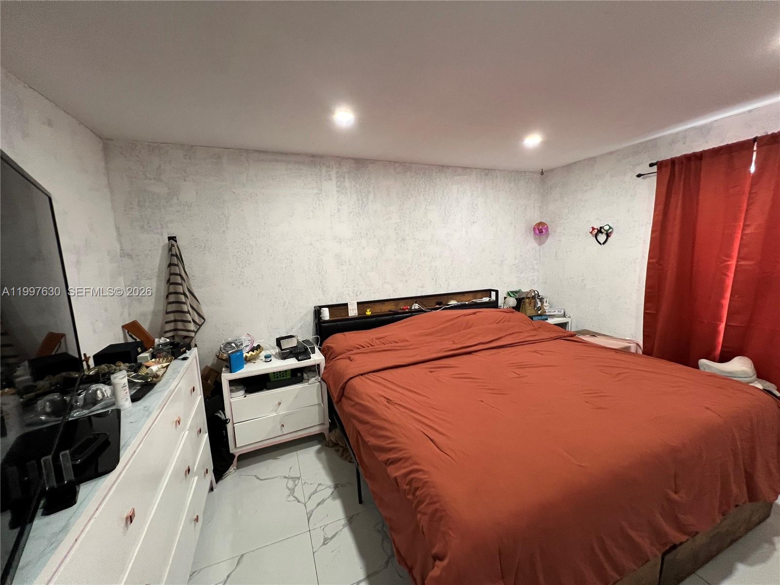 A bedroom features a bed with a rust-colored comforter, white dresser, and marble-patterned tile flooring — 450 NW 4th Ave, Homestead FL 33030, HOMESTEAD, FL