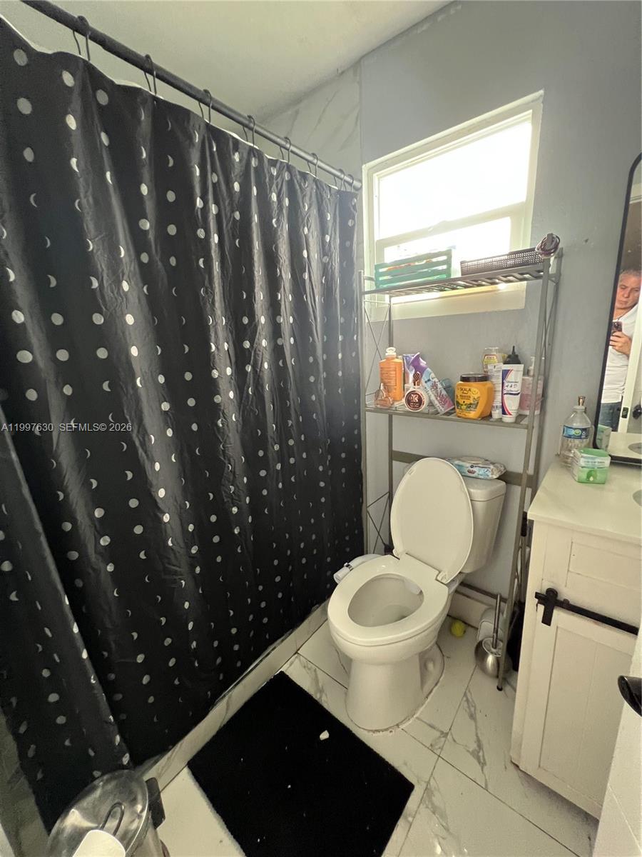 A bathroom features a black polka-dot shower curtain, a white toilet, and a metal storage rack — 450 NW 4th Ave, Homestead FL 33030, HOMESTEAD, FL