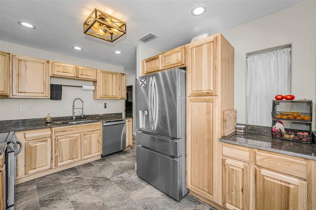 A kitchen features light wood cabinets, stainless steel appliances, dark countertops, and gray tile flooring — 5146 MALLETT DRIVE, PORT RICHEY, FL