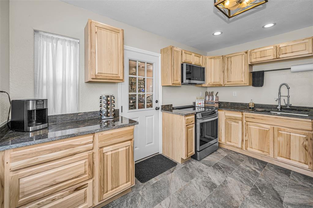 A kitchen with light wood cabinets, dark granite countertops, stainless steel appliances, and gray flooring — 5146 MALLETT DRIVE, PORT RICHEY, FL