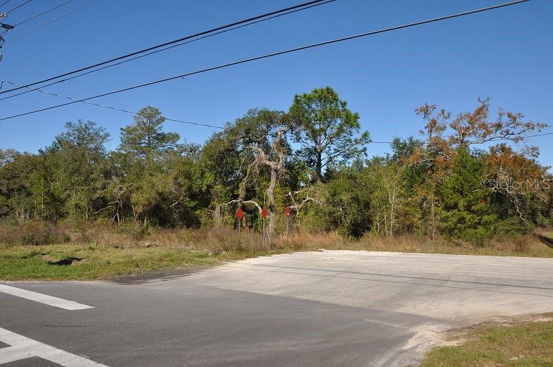 A paved road intersection meets a vacant, wooded lot under a clear blue sky — 11507 CORTEZ BOULEVARD UNIT 102, BROOKSVILLE, FL
