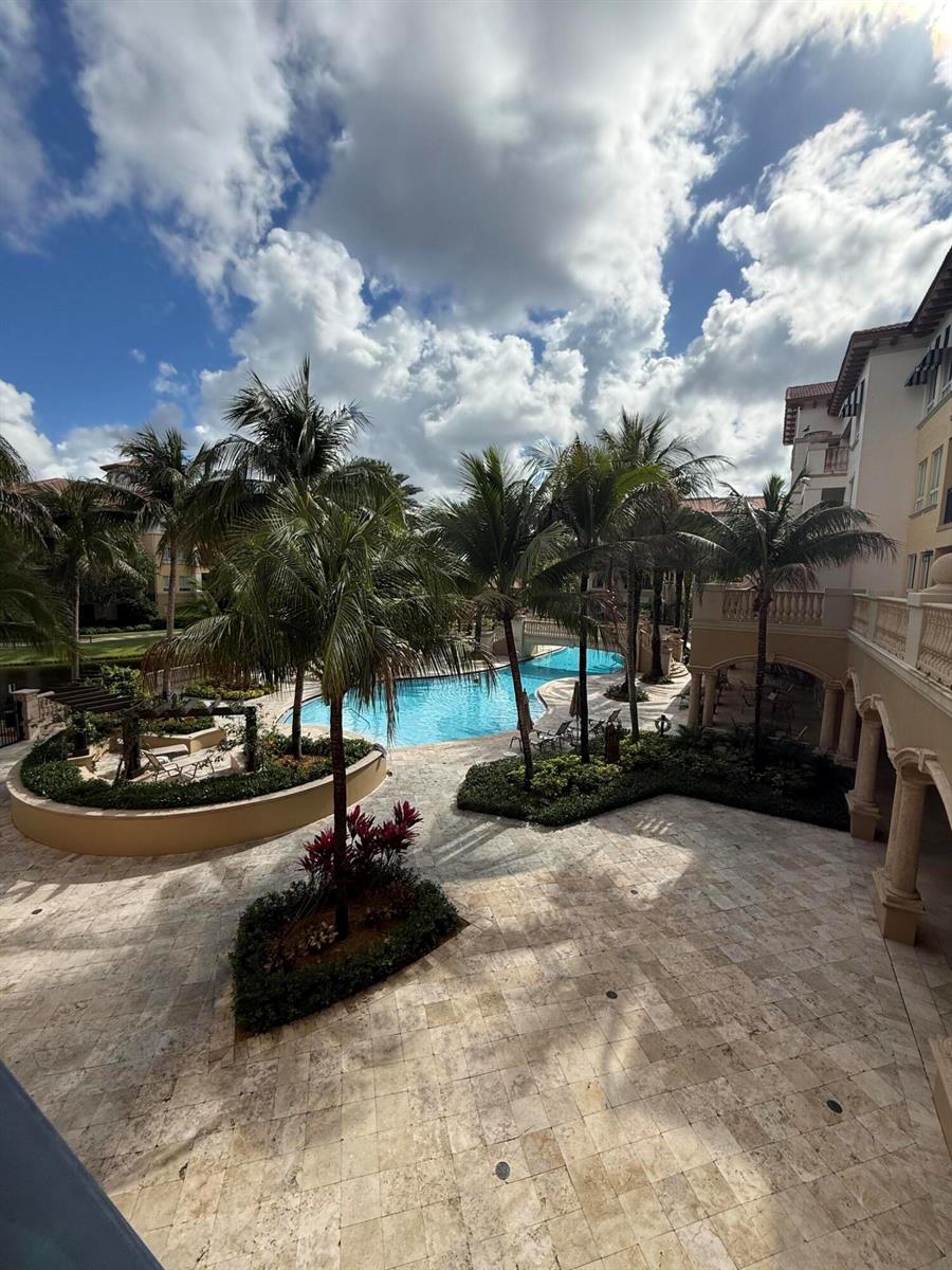 An elevated view of a resort-style swimming pool surrounded by palm trees and stone patios — 16102 Emerald Estates Drive # 212, Weston FL 33331, WESTON, FL
