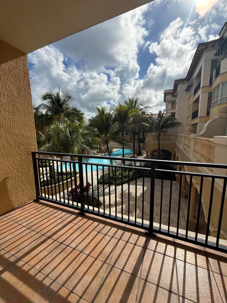 A balcony with tiled flooring and a black metal railing overlooks a swimming pool area — 16102 Emerald Estates Drive # 212, Weston FL 33331, WESTON, FL