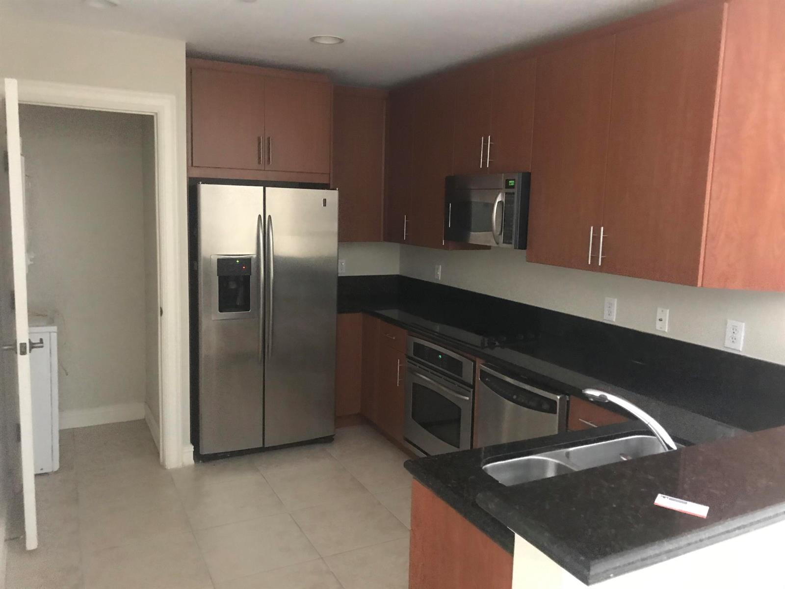 A kitchen featuring wood cabinets, black countertops, stainless steel appliances, and tile flooring — 16102 Emerald Estates Drive # 212, Weston FL 33331, WESTON, FL