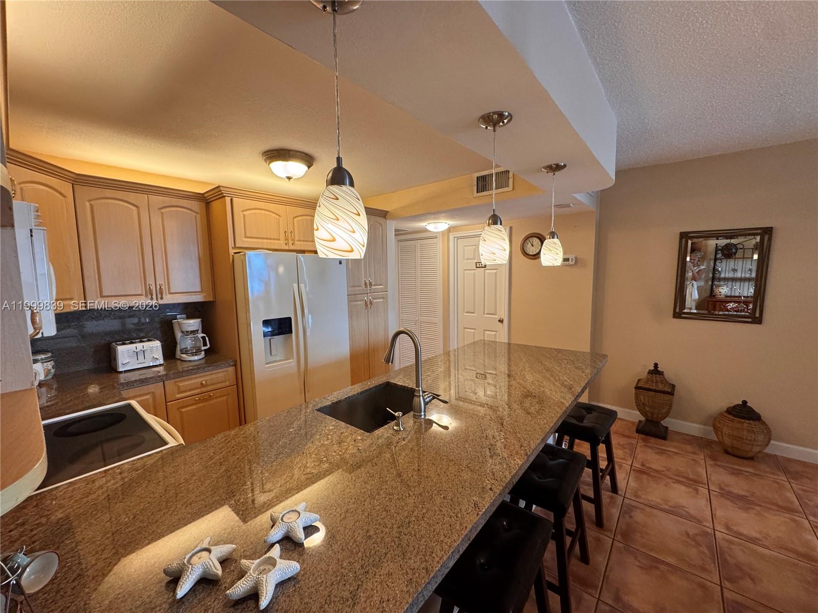A kitchen features light wood cabinets, granite countertops, a central island, and three pendant lights — 3725 S Ocean Dr # 421, Hollywood FL 33019, HOLLYWOOD, FL