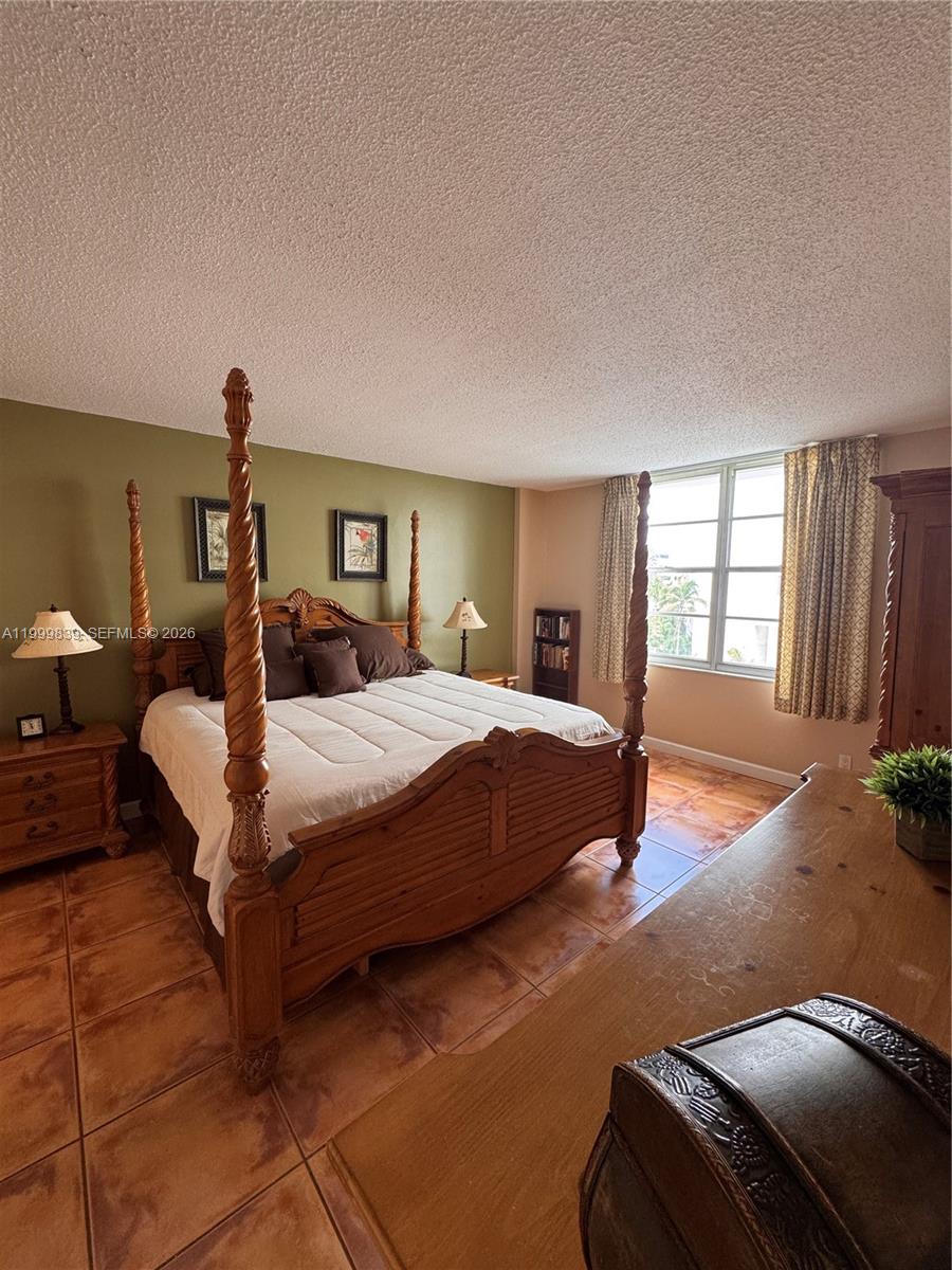 A bedroom features a four-poster wooden bed, tiled floors, and an olive green accent wall — 3725 S Ocean Dr # 421, Hollywood FL 33019, HOLLYWOOD, FL