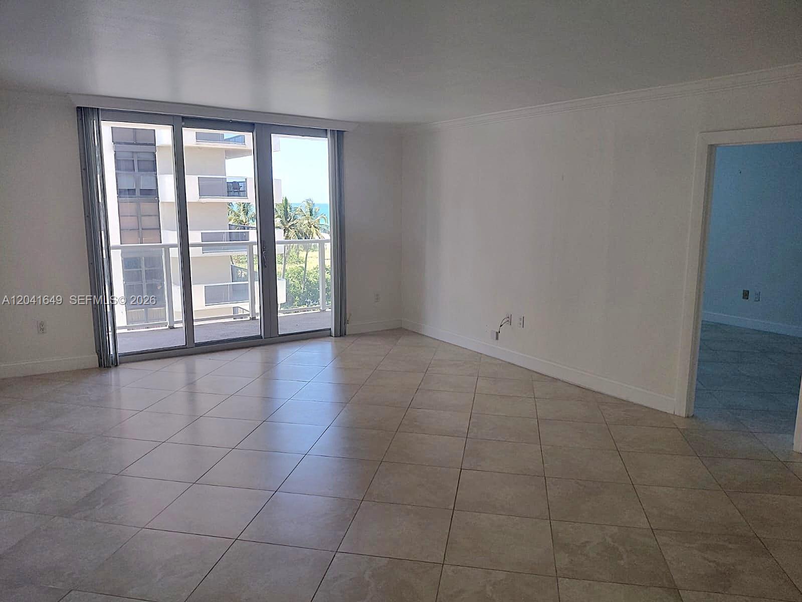 An empty living room features light-colored tile flooring, white walls, and a sliding glass door — 5701 Collins Ave # 619, Miami Beach FL 33140, MIAMI BEACH, FL