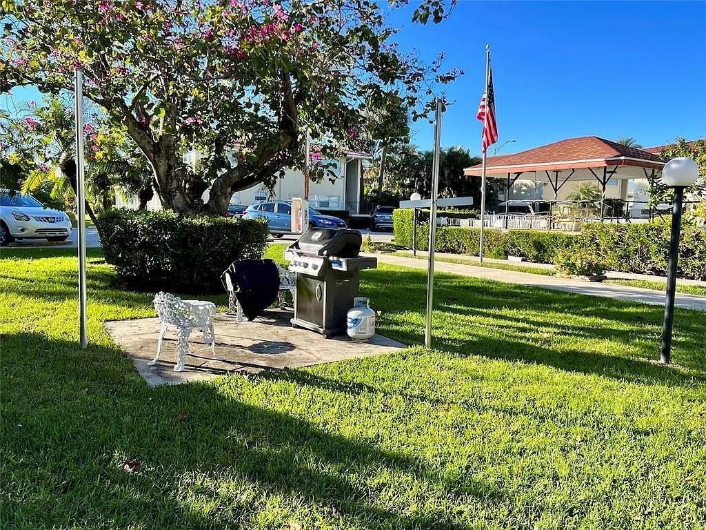 A grill and a white metal chair sit on a concrete pad under a tree — 2202 NE 36th Street # 15, Lighthouse Point FL 33064, LIGHTHOUSE POINT, FL