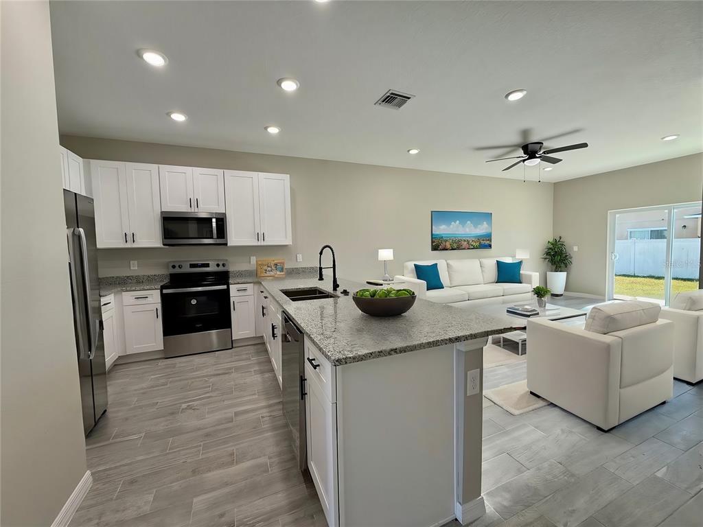 An open-concept kitchen with white cabinets and granite countertops overlooks a living room area — 703 CAMEL COURT, POINCIANA, FL