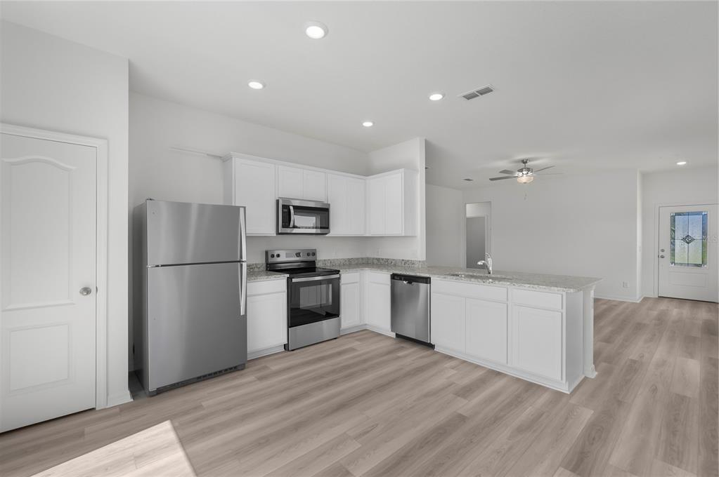 A modern kitchen features white cabinets, stainless steel appliances, granite countertops, and light wood flooring — 3715 BERGAMOT STREET, LAKE ALFRED, FL