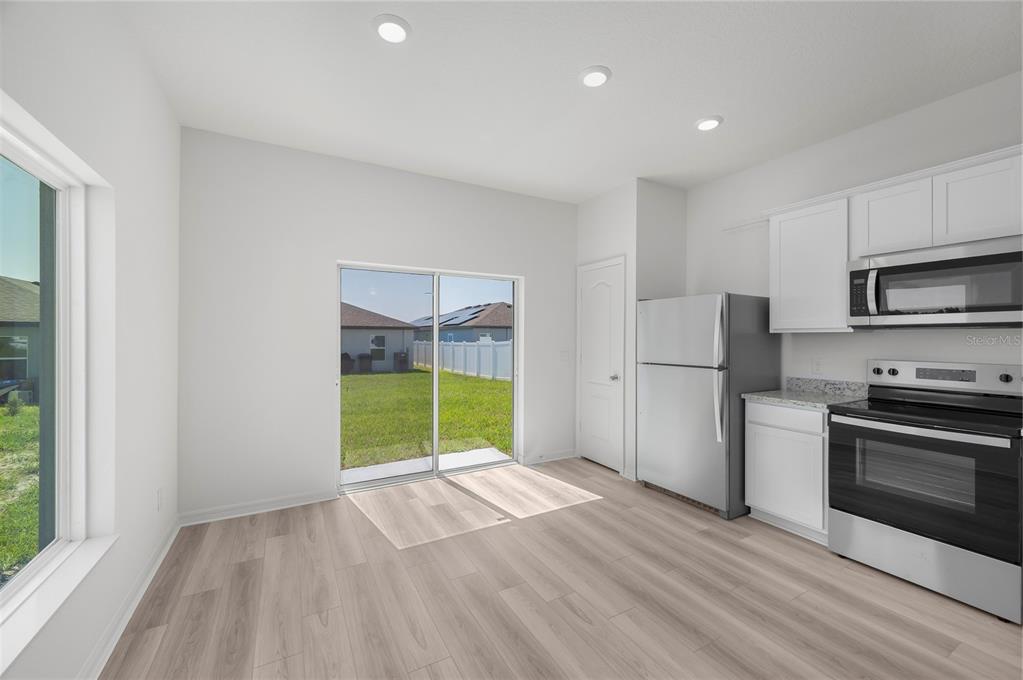 A kitchen with white cabinets, stainless steel appliances, light wood-look flooring, and a sliding glass door — 3715 BERGAMOT STREET, LAKE ALFRED, FL