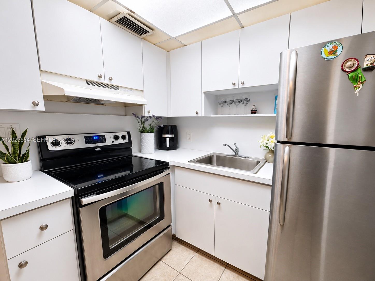 A compact kitchen features white cabinets, stainless steel appliances, and a single-basin sink — 447 NE 195th St # 115, Miami FL 33179, MIAMI, FL