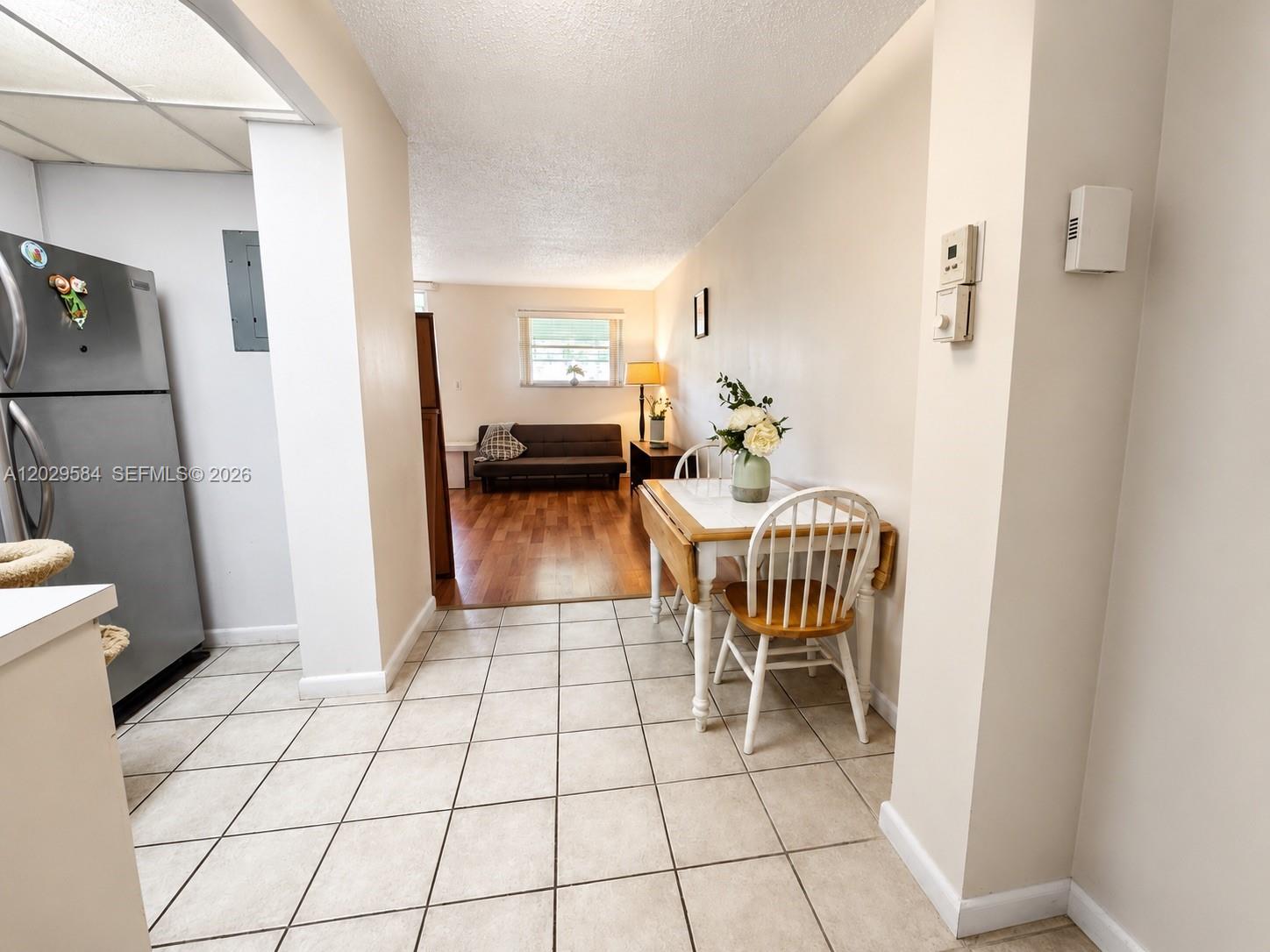 A tiled kitchen area opens into a living room with wood flooring and a sofa — 447 NE 195th St # 115, Miami FL 33179, MIAMI, FL