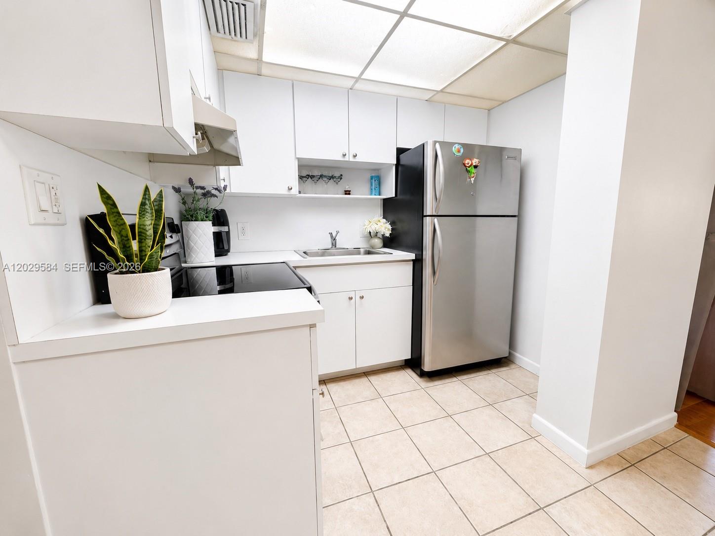 A small kitchen features white cabinets, stainless steel appliances, and light-colored tile flooring — 447 NE 195th St # 115, Miami FL 33179, MIAMI, FL