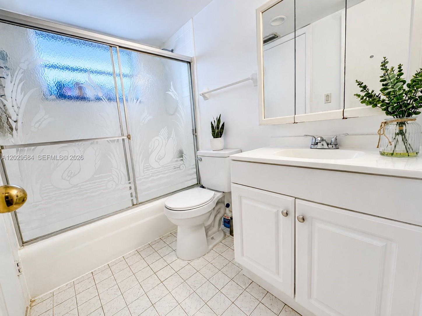 A bathroom features a white vanity, a toilet, and a bathtub with etched glass doors — 447 NE 195th St # 115, Miami FL 33179, MIAMI, FL