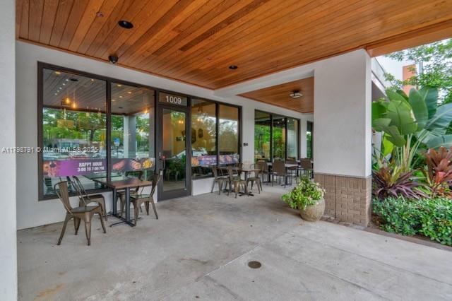 A covered outdoor patio area features tables, chairs, and large potted plants near a storefront — S University Dr, Plantation FL 33324, PLANTATION, FL