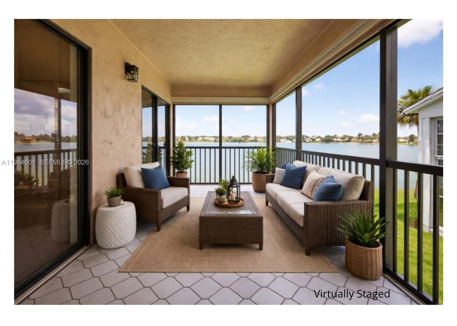 A screened-in patio with wicker furniture overlooks a lake, featuring tiled flooring and beige walls — 889 Hamilton Dr # 889L, Homestead FL 33034, HOMESTEAD, FL