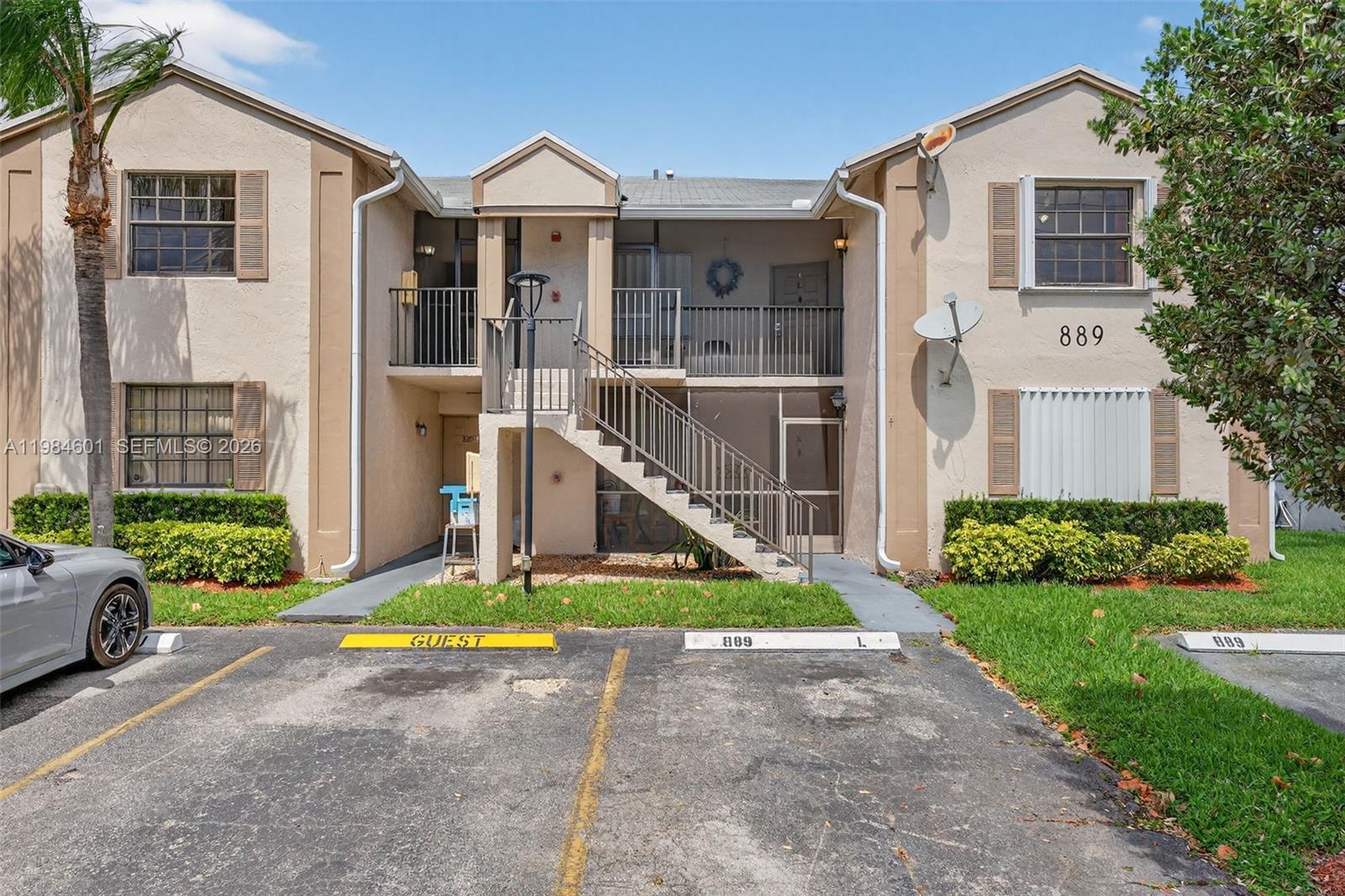 A two-story apartment building exterior features a central staircase, balconies, and designated parking spaces — 889 Hamilton Dr # 889L, Homestead FL 33034, HOMESTEAD, FL