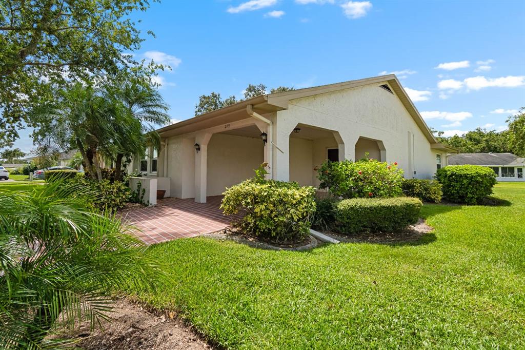 A single-story house exterior features a covered entryway, tiled patio, and landscaped front lawn — 2109 HARLESTON PLACE UNIT 2109, SUN CITY CENTER, FL