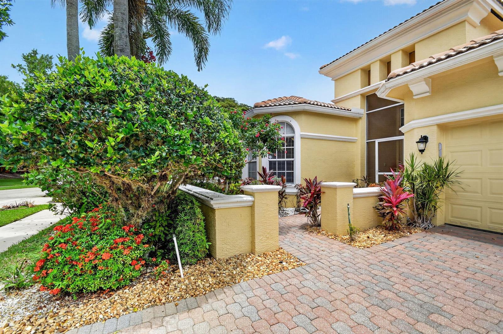 A yellow stucco house exterior features a brick paver driveway, landscaping, and a small courtyard — 1848 Via Castello, Wellington FL 33411, WELLINGTON, FL